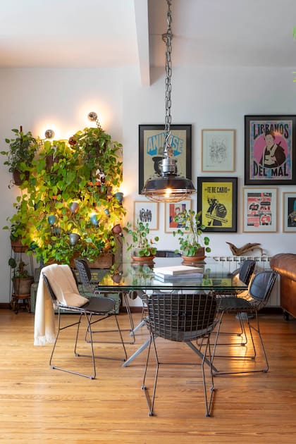 Mesa de comedor extensible con estructura de hierro y tapa de vidrio biselado, rodeada de sillas ‘Bertoia’. Dos lámparas galponeras enlozadas (Landmark), intervenidas con una malla metálica