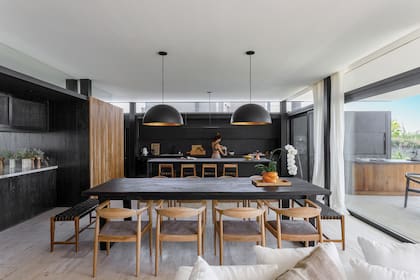 Mesa de kiri quemado con sillas ‘Kennedy’ y bancos con asiento tejido en cuero negro (todo de Carola Mauer). Las lámparas (Luz Buenos Aires).