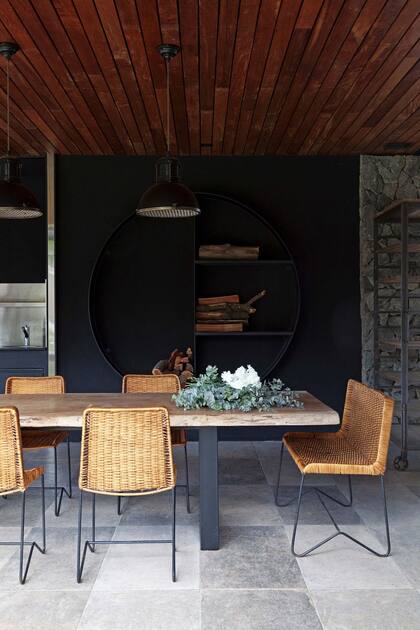 Mesa de timbó con patas de hierro, sillas de mimbre ‘Oveja’ (ambos de Mesopotamia BA) y lámparas galponeras (Costado). El leñero fue realizado por un herrero.