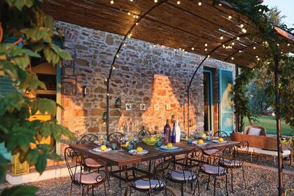 Mesa, sillas y arcos en hierro pintado en color óxido. Cuando la glicina pierde sus hojas, queda la protección de finas cañas de bambú.