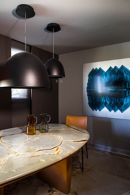 La tapa de la mesa fue realizada en cuarcita 'Blue Roma' (De Stefano) con un acabado cuarto de tabla en los bordes (Giannetta Mármoles). Sillas (Gris Dimensión). Lámparas Serafín (Idea Iluminación). Cuadro de Fernando Poggio (Diderot.art).