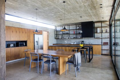 Mesada de Dekton ‘Domoos’ con amoblamiento enchapado en petiribí. Estanterías de hierro. La barra funciona como complemento de la mesa de madera maciza (todo de De Otro Tiempo) cuando la casa se llena de huéspedes.