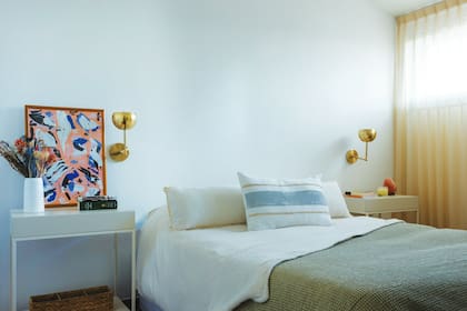 Mesas de luz laquedas (Alto Rancho), apliques de pared dorados (Sena Iluminación) y una ilustración son los únicos elementos en un ambiente por demás despojado. Almohadón pintado a mano (LV Concepto Interior).