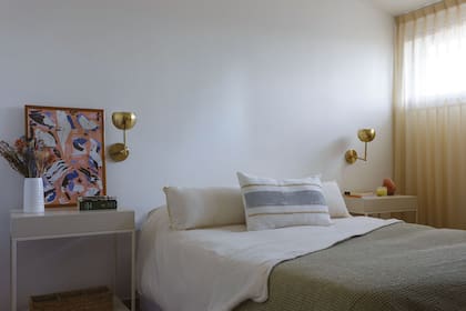 Mesas de luz laquedas (Alto Rancho), apliques de pared dorados (Sena Iluminación) y una ilustración son los únicos elementos en un ambiente por demás despojado. Almohadón pintado a mano (LV Concepto Interior).