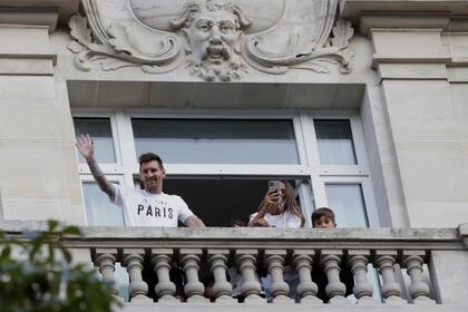 Messi saluda a sus seguidores desde el balcón de su hotel mientras su esposa, Antonela Roccuzzo, toma fotografías: ocurrió en París, el 10 de agosto, cuando iniciaron su nueva vida