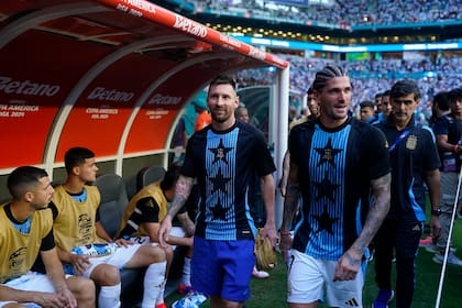 Messi y De Paul ríen, camino al banco