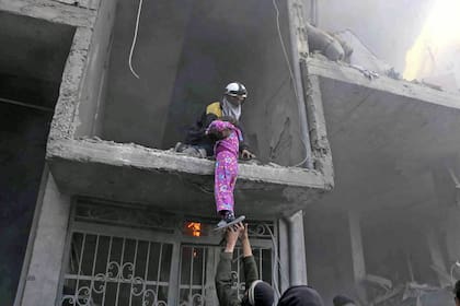 Miembros de la Defensa Civil Siria ayudan a sacar a una chica de los escombros, tras los bombardeos en Ghouta Oriental