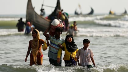Refugiados Rohingya caminan a la orilla con sus pertenencias después de cruzar la frontera de Bangladesh-Myanmar en barco a través de la bahía de Bengala