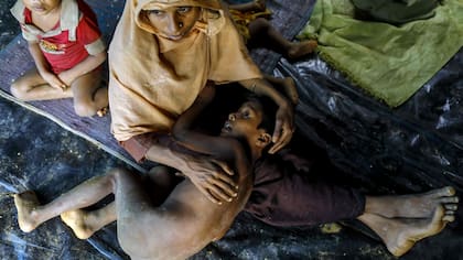 Un refugiado Rohingya de Myanmar sostiene a un niño mientras se sienta en un refugio improvisado cerca de la ciudad de Teknaf, Bangladesh