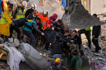 Miembros de un equipo de emergencia transportan el cuerpo de una persona hallado entre los escombros de un edificio destruido en Adana, Turquía, el martes 7 de febrero de 2023.