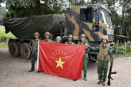 Miembros del Ejército de la Alianza Democrática Nacional de Myanmar con la bandera del grupo posan para una fotografía delante de un camión militar incautado en el municipio de Kunlong, en el estado de Shan, Myanmar, el domingo 12 de noviembre de 2023. (El medio de comunicación en línea Kokang vía AP)