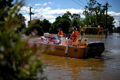 Miembros del Servicio de Emergencia del Estado transportan artículos de socorro durante las operaciones de rescate en un área residencial inundada en el suburbio de Windsor en el noroeste de Sydney
