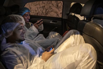 Los trabajadores de la funeraria Piedrangel, el venezolano Luis Zerpa y el peruano Angelo Aza, juegan en sus celulares mientras esperan el cuerpo de una persona que murió por coronavirus, frente al Hospital de Emergencia de Villa El Salvador en Lima