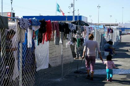 Migrantes caminan a lo largo de una cerca en un campamento improvisado que es hogar temporal de cientos de migrantes que esperan solicitar asilo en Estados Unidos en un cruce peatonal el 8 de noviembre de 2021, en Tijuana, México. (AP Foto/Gregory Bull, Archivo)