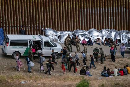 Migrantes caminan hacia un vehículo para ser procesados por autoridades estadounidenses en el lado estadounidense de la frontera entre México y Estados Unidos, visto desde Tijuana, estado de Baja California, México, el 11 de mayo de 2023.