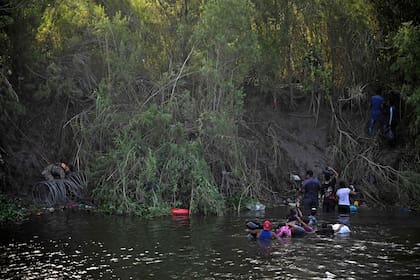 Migrantes cruzan el río Bravo mientras miembros de la Guardia Nacional de EE. UU. colocan una barrera de alambre de púas a lo largo del río en la frontera entre EE. UU. y México, visto desde Matamoros, estado de Tamaulupas, México, el 10 de mayo de 2023