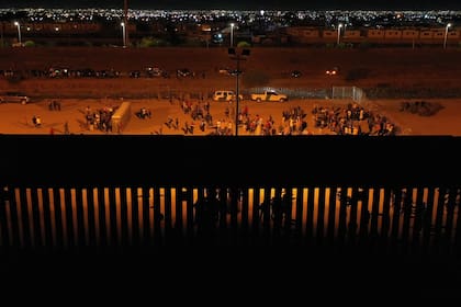 Migrantes esperan de noche a lo largo del muro fronterizo para entregarse a los agentes de la Patrulla Fronteriza de Aduanas y Protección Fronteriza (CBP) de EE. UU. para el procesamiento de solicitudes de asilo e inmigración antes de que expire el Título 42 al cruzar el río Grande desde Ciudad Juárez (TOP) hacia los Estados Unidos en la frontera entre Estados Unidos y México en El Paso, Texas, el 11 de mayo de 2023