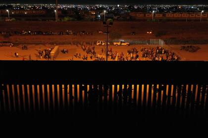 Migrantes esperan de noche junto al muro fronterizo que separa México de Estados Unidos.