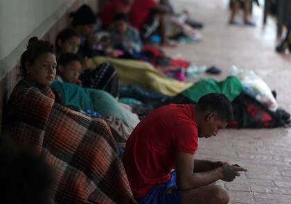 Migrantes venezolanos sentados junto a la pared de un edificio mientras se resguardan de la lluvia, en Matamoros, México, el sábado 13 de mayo de 2023 (AP Foto/Fernando Llano)