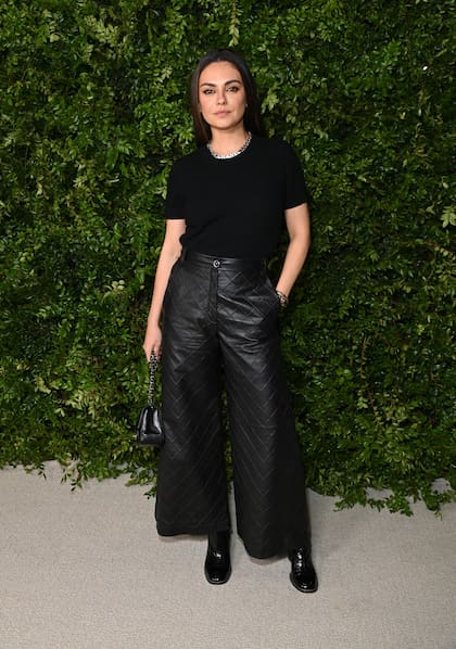 Mila Kunis se decantó por un look total black de remera manga corta, pantalón de cuero acolchado, botas de charol y minibolso a tono, aunque aportó brillo con un collar de cadenas