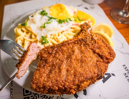 Milanesa con hueso, servida con fideos a la carbonara y huevo jugoso