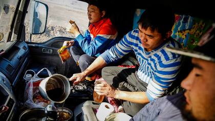 Tres hombres comen una cena de fideos instantáneos y carne seca dentro de un camión en Khanbogd Soum