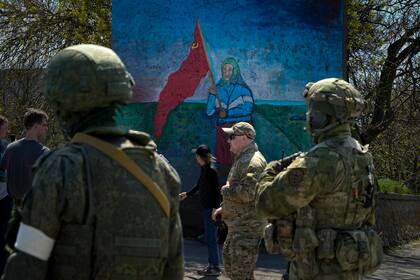 Militares rusos cerca de una pintura de una mujer ucraniana que sostiene una bandera roja de la era soviética en el territorio bajo el gobierno de la República Popular de Donetsk, en el este de Ucrania, el sábado 30 de abril de 2022. 