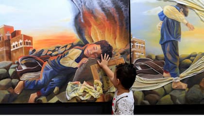 Un chico yemení posa su mano sobre una de las pinturas expuestas