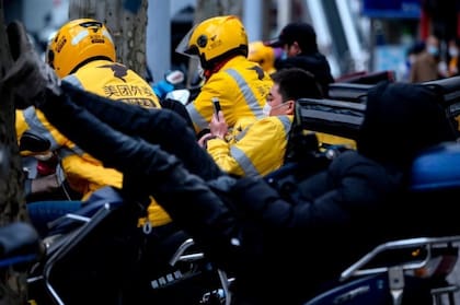 Motociclistas que hacen entregas a domicilio esperan a que les lleguen los pedidos en una calle en Shanghái