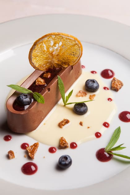 Mousse de chocolate sobre base de biscuit con coulis de arándanos y calafate, con crocante de almendras y naranjos.