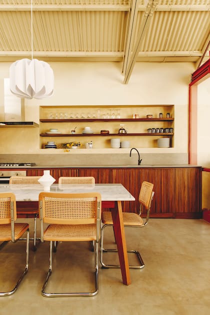 Mueble bajomesada con frente varillado (Eme Carranza), estructura que se repite para contener la heladera (Samsung). Mesa con tapa de mármol (Canteras del Mundo). Sillas (Landmark). Piso de hormigón alisado.