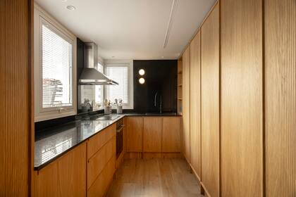 Mueble bajomesada de roble americano, placar de roble americano ranurado (todo diseñado a medida por Alejandra Nusenovich). Mesada de granito 'Negro Brasil'. Apliques de pared (Huup).