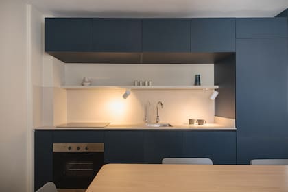 Mueble de melamina ‘Taureg’ (Faplac) diseñado por el Estudio, con mesada y alzada de Purastone ‘Lime Stone’ (Marmolería Gaona). Bacha ‘Quadra Q40’ (Johnson Acero), grifería mocomando ‘Puelo’ (FV). Anafe (Teka) y horno (Longvie), eléctricos. En el estante, artefactos de iluminación ‘h 473’ de Huup (Griscan).