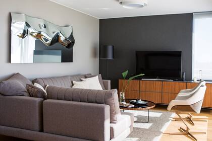 Mueble de TV, sillón 'Mercury', espejo-cuadro de diseño italiano (todo de Walmer). Lámpara 'Hi Hat' con pantalla negra (Kikely). Plafón dimerizable (Griscan). Pisos de roble de Eslavonia (Patagonia Flooring).