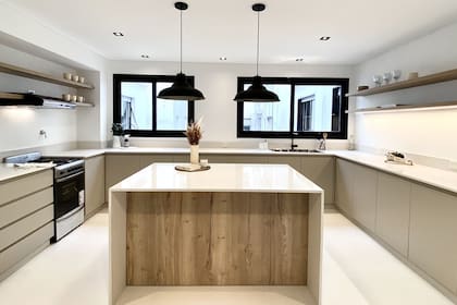 Mueble laqueado, mesada 'Blanco Norte' (Silestone) y lámparas (Omniluz). Estantes y frente de la isla en melamina 'Roble Halifax Natural' (Egger). De gran formato, el piso de porcellanato 'Basaltina White' (Vite) abre y amplia el espacio.