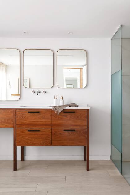 Mueble (Muchnik y Wainstein) enchapado en petiribí con mesada de Silestone ‘Miami White’ (Canteras del Mundo) con bacha (Roca) y grifería de pared (FV). Dispenser y vaso (Philippa Deco Boutique). Espejos diseñados y ejecutados a medida.