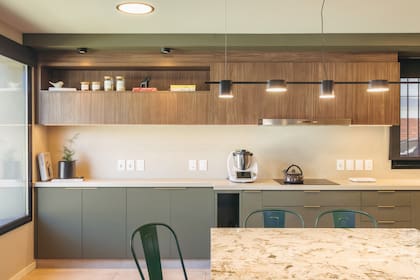 Muebles bajos en MDF Safari (FaPLac) con tiradores dorados mate y mesada Dekton Danae. Mesa con tapa en granito Alpinus y sillas Tolix. Luces colgantes (Unik Punta del Este).