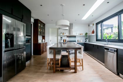 Muebles de cocina de frente enchapado en negro (Occhipinti). Vajillero de lenga y mesa central a medida (Estudio FH). Lámparas de techo (DIMM Iluminación).