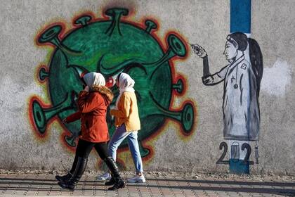 Mujeres palestinas pasan al lado de un mural de una enfermera que inyecta la vacuna contra el Covid-19 en la Ciudad de Gaza, el 31 de diciembre de 2020