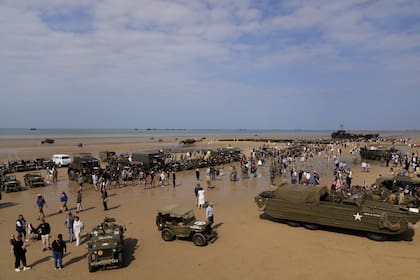 Multitudes rodean vehículos conducidos por varios vehículos propiedad de recreadores en la playa, mientras participan en un desfile de vehículos de la Segunda Guerra Mundial en el 80 aniversario del Día D en Arramanches les-Bains en Normandía, Francia, el jueves 6 de junio de 2024. 