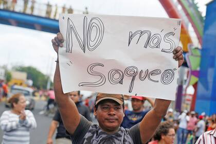 Un hombre sostiene un cartel con la leyenda "no más saqueo", en medio de las violentas protestas