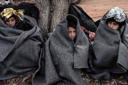 Niños con mantas se sientan en la playa después de que un bote con 54 refugiados afganos desembarcó en la isla griega de Lesbos