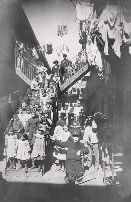 Niños en la escalera de un conventillo.
La cara del señor sentado estaba alterada en el original en el AGN. s/d.