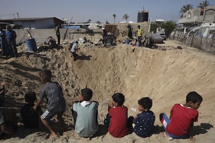 Niños palestinos sentados al borde de un cráter tras un ataque aéreo israelí en Khan Younis, sur de la Franja de Gaza, viernes 21 de junio de 2024.