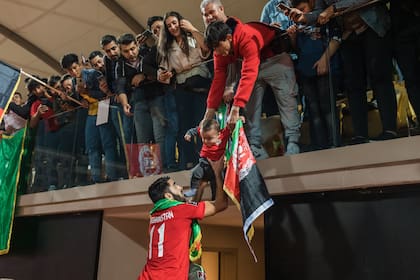 Norlla Amiri, de la selección nacional de fútbol de Afganistán, usa a un compañero de equipo para alcanzar a su hijo recién nacido entre los fanáticos afganos, después del amistoso internacional con Indonesia en el Gloria Sports Arena en Antalya, Turquía