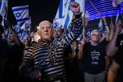 Numerosas personas, entre ellas una disfrazda del primer ministro israelí Benjamin Netanyahu encadenado, protestan contra los planes del gobierno de modificar el sistema judicial, durante una movilización en Tel Aviv, Israel, el sábado 10 de junio de 2023. (AP Foto/Tsafrir Abayov)