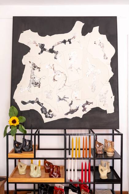 Obra 'País Lejano' en cuero reciclado cosido e intervenido con técnica mixta, montado sobre tela pintada de negro y enmarcado en kiri negro. Debajo, sus objetos fluidos hechos artesanalmente en cerámica.