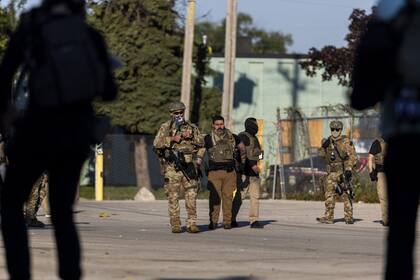 Oficiales del Servicio de Control de Inmigración y Aduanas (ICE) vigilan en medio de protestas para asegurar un área frente a una instalación en Chicago