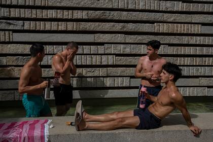 Jóvenes se refrescan en un parque junto a un río de Madrid