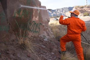 Operarios con hidrolavadoras trabajan esta tarde en la limpieza de los nombres que dejaron estampados con pintura en aerosol al menos tres turistas del conurbano bonaerense en rocas del Dique Potrerillos